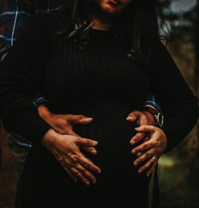 Black man and black woman holding their hands lovingly over the woman's clearly pregnant stomach. Black maternal health disparities and primary care.