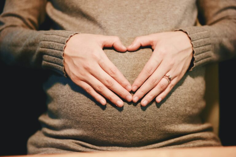 pregnant woman belly with hands in the shape of a heart on the belly.