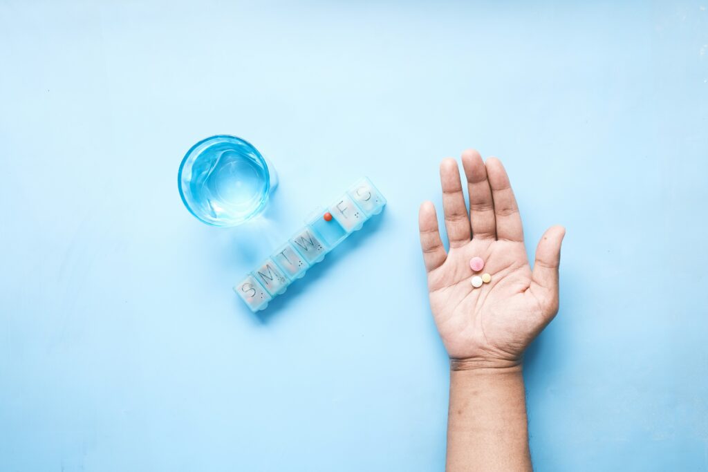 blue background, human hand laying palm up holding anxiety medication, 3 pills, next to a blue pill box and blue glass of water