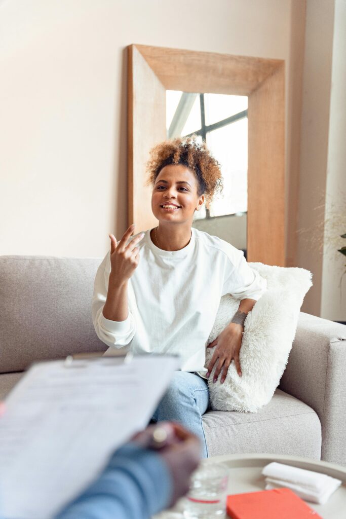 Woman sitting on chair happily talking with a therapist off-camera with a clipboard - How to Start Therapy